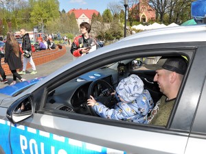 w policyjnym radiowozie siedzi mężczyzna, ma na kolanach malutkie dziecko, które trzyma kierownicę