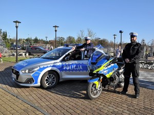 policjanci stoją obok policyjnego motocykla i radiowozu, uśmiechają się