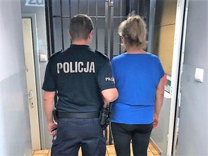 policjant trzyma kobietę, która ma założone na ręce kajdanki, stoją tyłem