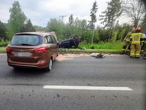 na jezdni stoi rozbity samochód, obok stoją strażacy