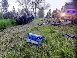 na poboczu leży na dachu rozbity samochód, obok niego stoją strażacy i porozrzucane części samochodu