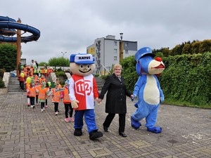 Na zdjęciu widać kobietę trzymająca za ręce maskotki, a za nimi idą dzieci w parach.