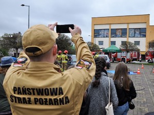 Zdjęcie przedstawia strażaków, którzy przedstawiają jak wydostać osobę poszkodowaną z samochodu.