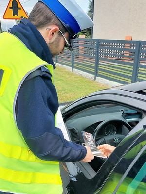 Policjant wręcza kierującemu samochód ulotkę związaną z ograniczeniem prędkości