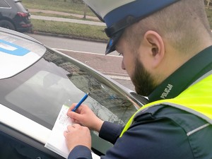 Na zdjęciu znajduje się policjant wypisujący mandat.