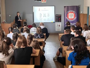 młoda kobieta prowadzi spotkanie profilaktyczne, na sali w ławkach siedzi młodzież