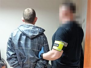 Na zdjęciu widać mężczyznę, obok widać nieumundurowanego policjanta, mężczyźni stoją tyłem.