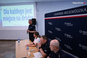 Na zdjęciu widać trzech policjantów oraz kobietę z czego jeden z policjantów przemawia, a pozostałe osoby siedzą przy stole