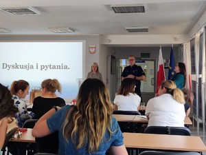 Na zdjęciu widać osobę, która przemawia do zgromadzonych osób oraz policjanta, który stoi tuż obok.