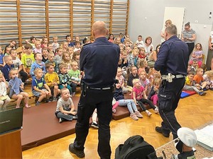 policjanci stoją przed grupą dzieci podczas spotkania profilaktycznego