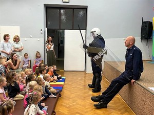 policjanci stoją przed siedzącymi dziećmi podczas spotkania profilaktycznego