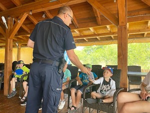 Zdjęcie przedstawia policjanta, który wręcza małemu chłopcu nagrodę za poprawnie udzielona odpowiedź.