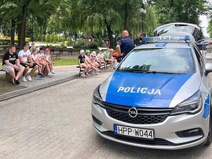 Na zdjęciu widać radiowóz, dzieci oraz policjantów, którzy przypominają im o zasadach jakie należy przestrzegać podczas wakacji