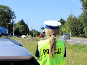 obok radiowozu stoi policjantka, obserwuje ruch pojazdów