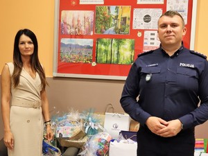 na zdjęciu I Zastępca Komendanta Powiatowego Policji w Wodzisławiu Śląskim pozuje do wspólnego zdjęcia z Dyrektor Domu Dziecka w Gorzyczkach, za nimi znajdują się torby z prezentami dla dzieci