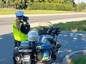 policjantka stoi obok policyjnego motocykla, kontroluje prędkość, z jaką poruszają się pojazdy