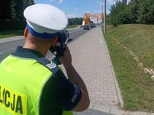 policjant stoi przy drodze i mierzy prędkość, z jaką poruszają się pojazdy