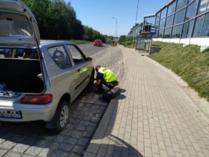 Zdjęcie przedstawia policjanta wymieniającą uszkodzone koło w pojeździe.