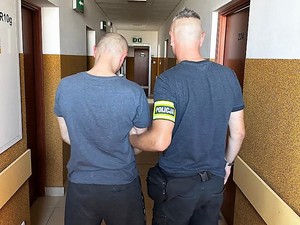 nieumundurowany policjant trzyma za rękę zatrzymanego mężczyznę, obaj stoją tyłem