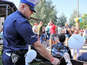 policjant stoi przed grupą osób podczas koncertu Powiatowy Blues, przekazuje balon uczestniczce koncertu