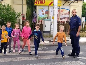 policjant asekuruje grupę dzieci, które przechodzą przez jezdnię