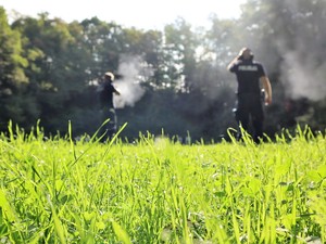 policjant strzela z broni długiej do tarczy, obok niego stoi policyjny instruktor strzelań