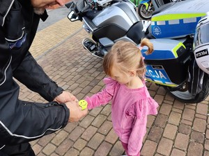 policjant zakłada na rękę dziewczynki opaskę odblaskową