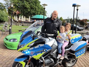 policjant stoi obok motocykla, na motocyklu siedzi dziecko