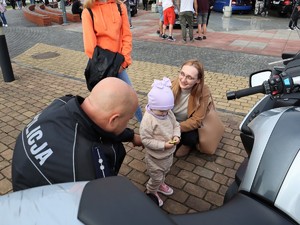 policjant kuca obok małej dziewczynki, która trzyma w ręku odblask