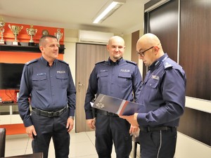 Komendant Powiatowy Policji w Wodzisławiu Śląskim wręcza list gratulacyjny wyróżnionemu policjantowi, obok niego stoi jego przełożony, Komendant Komisariatu Policji w Gorzycach