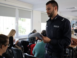 policjant dzielnicowy rozdaje uczestnikom debaty ankiety