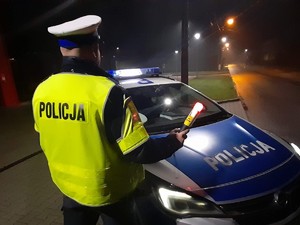 na tle radiowozu stoi policjant trzymający alkomat, zdjęcie wykonane jest nocą