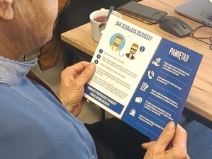 na zdjęciu widać seniora, który trzyma ulotkę informacyjną o metodach działania oszustów