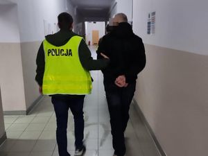 policjanci idący korytarzem prowadzą zatrzymanego mężczyznę