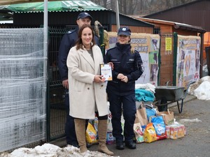 obok zebranych darów dla schroniska dla zwierząt stoją policjanci oraz pracownik przedszkola