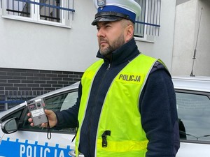 policjant trzyma w ręku alkomat, stoi obok radiowozu