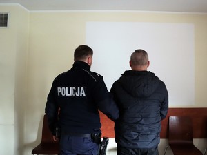 policjant trzyma pod ramię zatrzymanego mężczyznę, stoją tyłem