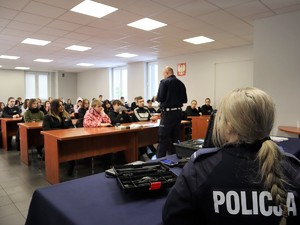 policjant prowadzi spotkanie profilaktyczne z młodzieżą, za nim siedzi policjantka, przygląda się