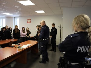 policjant prowadzi spotkanie z młodzieżą, za nim stoi policjantka