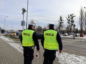 policjanci stoją przy przejściu dla pieszych, obserwują ruch samochodów