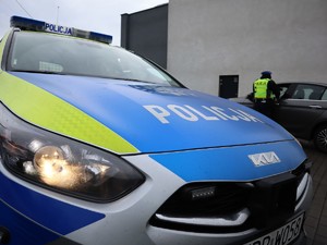 na zdjęciu widać policyjny radiowóz oraz policjanta w tle, który kontroluje samochód