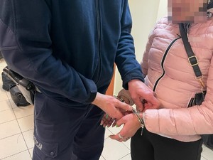 policjant odpina kluczykiem kajdanki, które ma na rękach założone zatrzymana kobieta