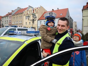 policjant stoi obok radiowozu, trzyma na rękach chłopczyka