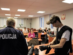 praktykant ubiera policyjny strój bojowy, obok niego stoi policjant
