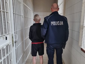 tyłem stoi policjant oraz zatrzymany za zabójstwo mężczyzna