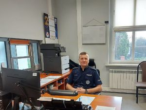 zdjęcie przedstawia siedzącego za biurkiem policjatna
