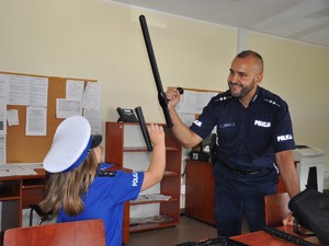 policjant i dziewczynka w stroju policjantki stoją na przeciwko siebie, trzymają w rękach pałki