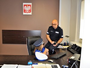 komendant siedzi obok ubranej w strój policjanta dziewczynki, pokazuje jej policyjną radiostację