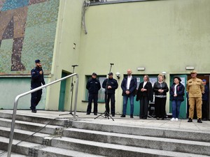 na schodach stoją w szeregu oficjalni goście w tym policjanci i strażak