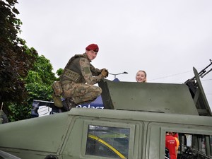 żołnierz kuca obok uśmiechniętej dziewczyny, która znajduje się w pojeździe wojskowym